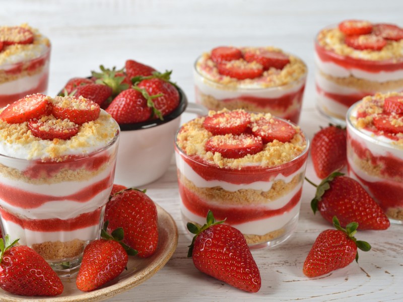 Dessertgläser mit Erdbeeren, Käsekuchenfüllung und gekrümelten Keksen.