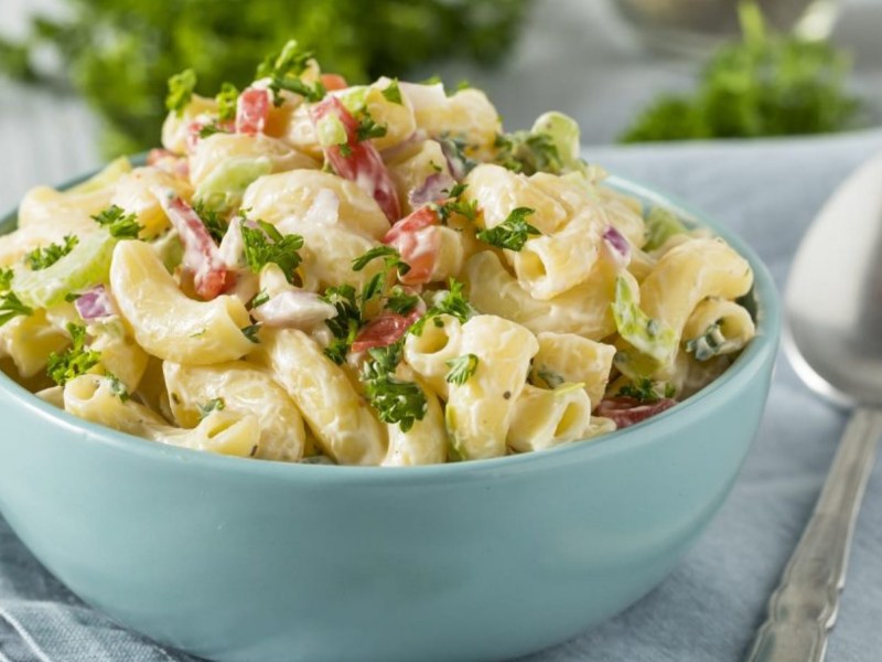 Nudelsalat in einer hellblauen Schüssel mit Petersilie und Speck.