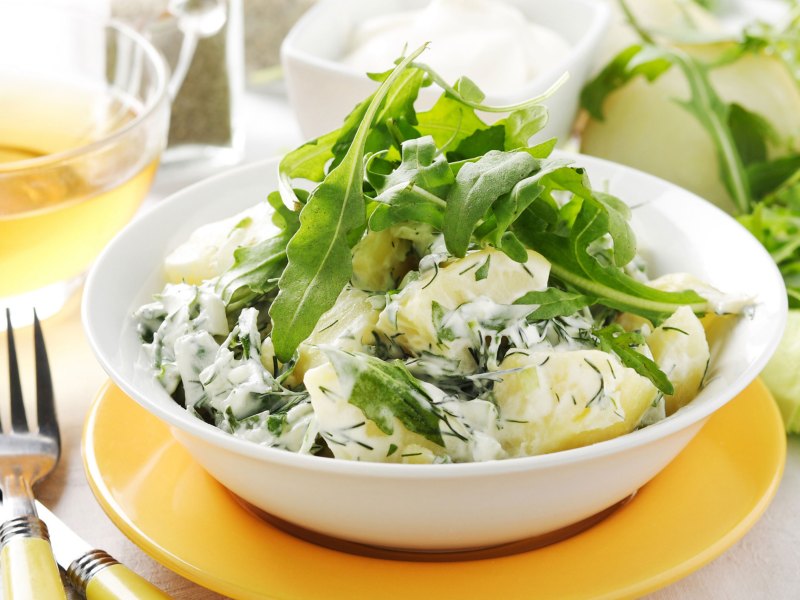 Kartoffelsalat mit Joghurtdressing und Rucola in wei&szlig;er Sch&uuml;ssel.