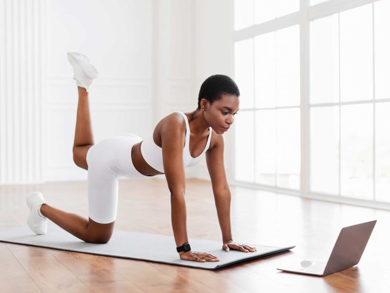Fitnesstraining zu Hause: Sportliche Frau in wei&szlig;er Trainingsbekleidung folgt einem Online-Fitness-Kurs in einem hellen Raum.