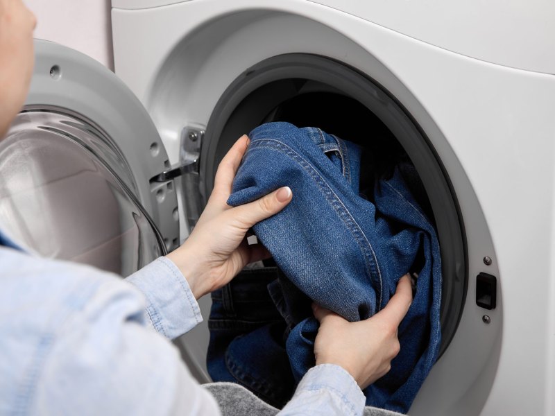 Frau, die eine Waschmaschine mit Jeanshosen bef&uuml;llt