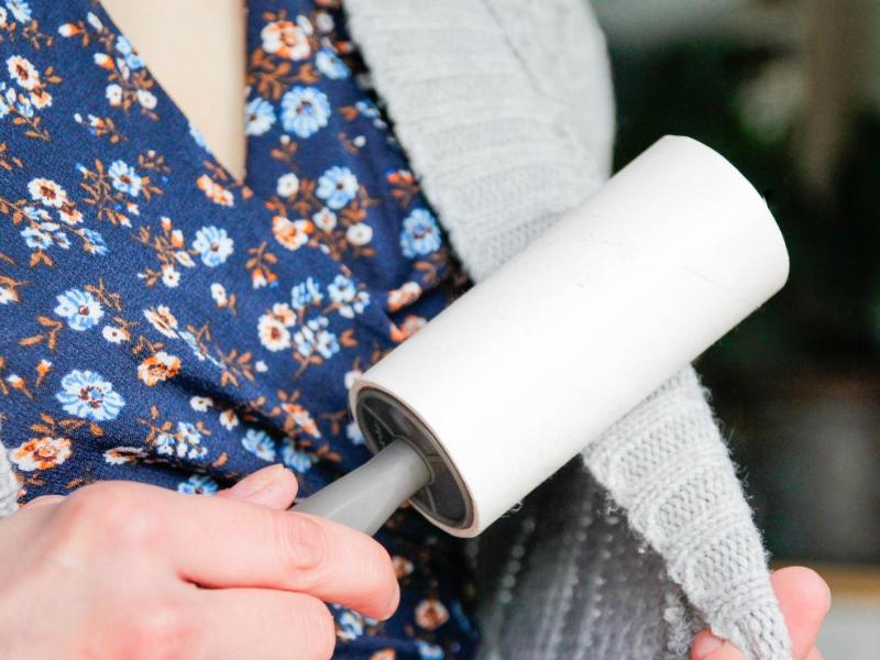 Frau entfernt Fusseln auf einer Strickjacke mit einer Fusselrolle.
