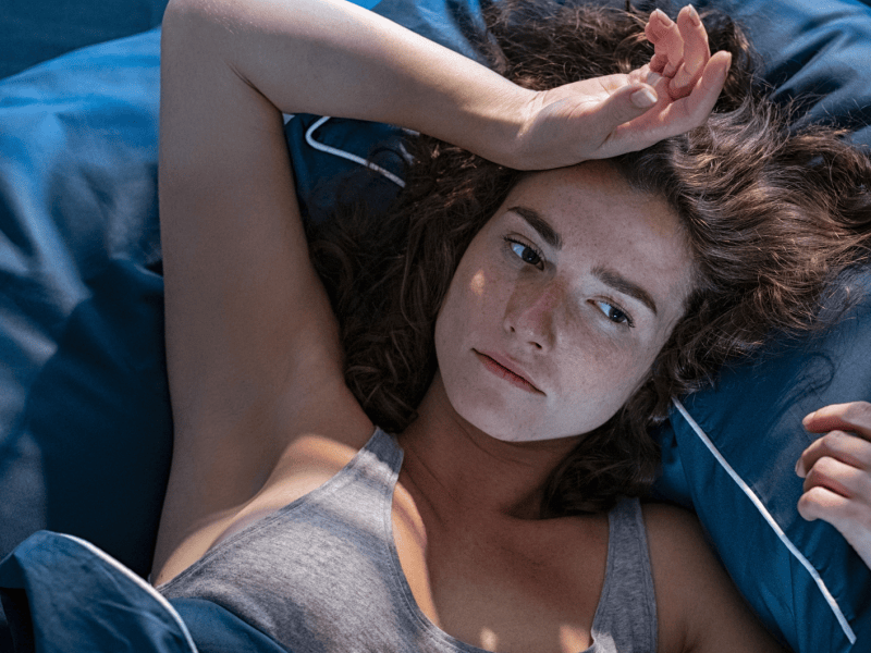 Frau im Bett, die sich nachdenklich und erschöpft auf die Stirn packt.