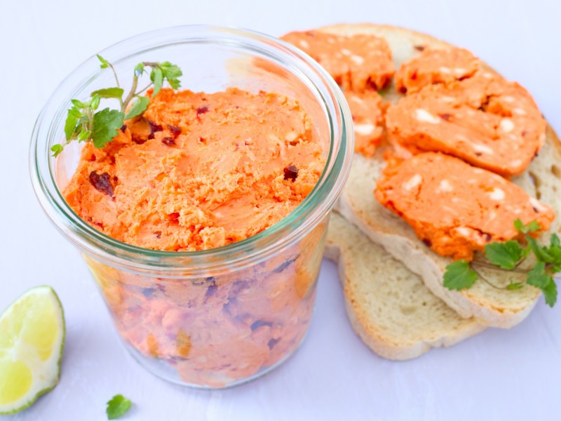 Tomatenbutter in einem Glasgef&auml;&szlig;, daneben zwei Scheiben Brot mit Tomatenbutter.