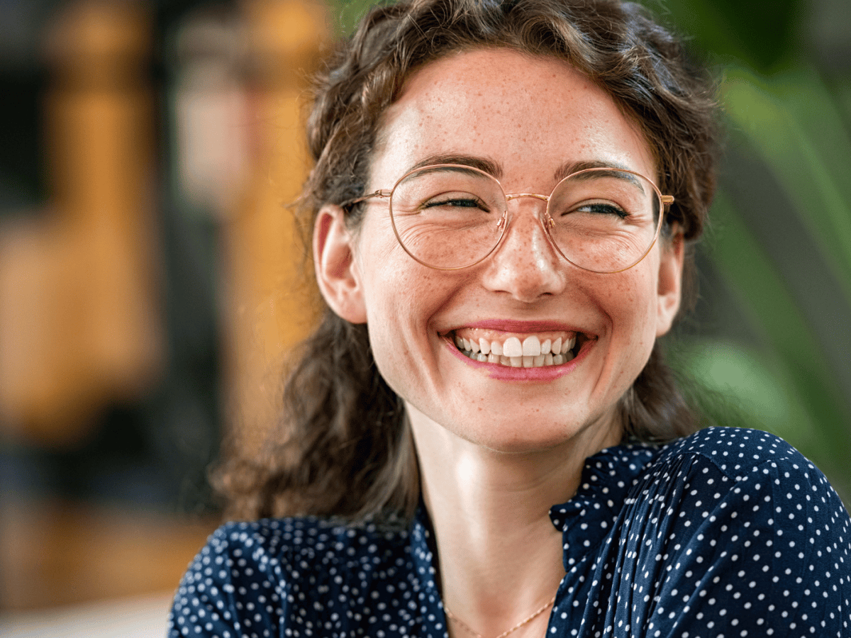 Junge Frau mit Brille l&auml;chelt breit.