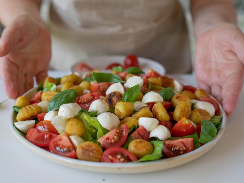 Salat mit Gnocchi, Tomaten, Mozzarella und Basilikum in einer gro&szlig;en Schale.
