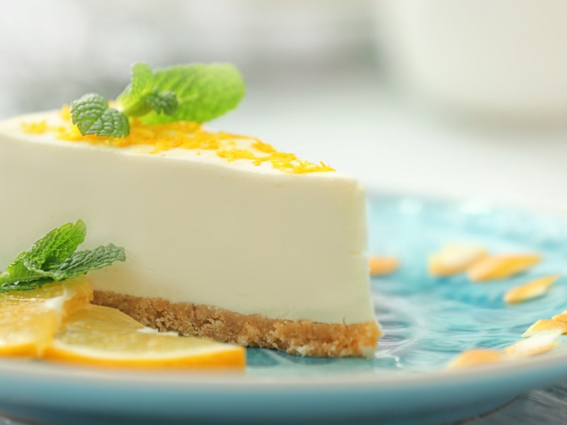 Frischk&auml;se-Zitronen-Torte mit Keksboden auf einem t&uuml;rkisen Teller.