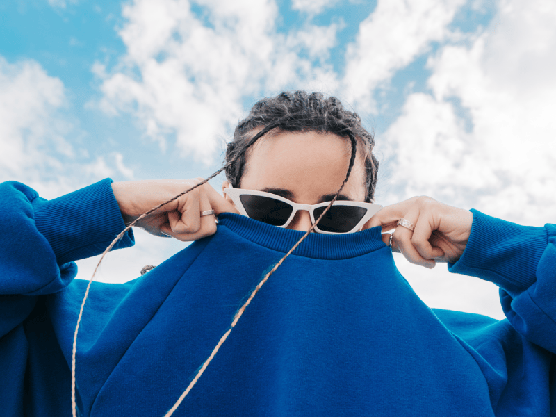 Frau mit Sonnenbrille versteckt ihr Gesicht in ihrem Pullover