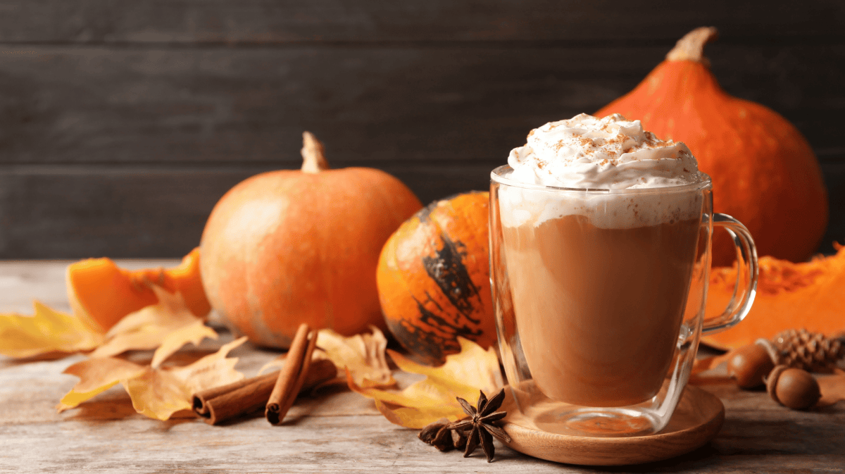 Glasbecher mit einem leckeren Kürbis-Gewürz-Latte auf einem Holztisch 