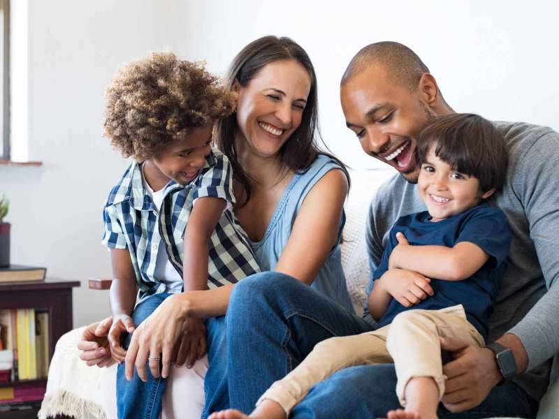 Mann und Frau sitzen mit ihren zwei Kindern auf der Couch und lachen.