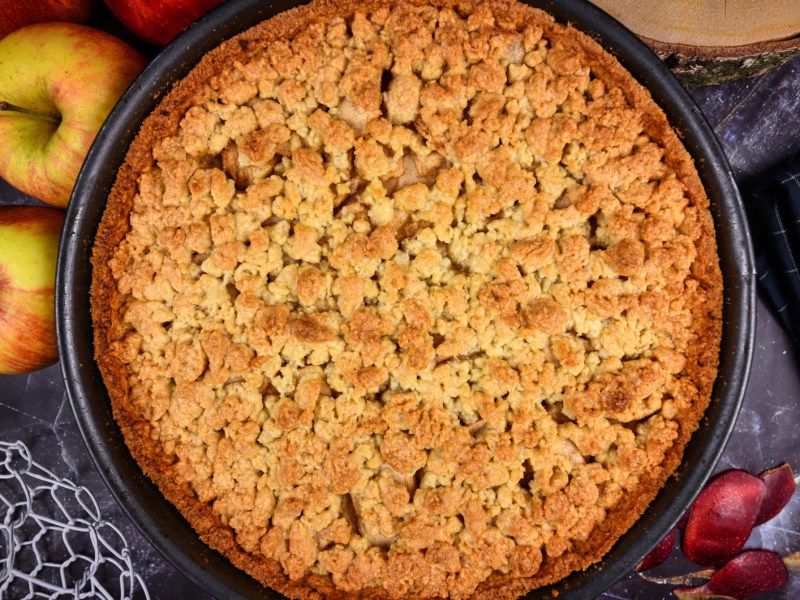 Apfelkuchen mit Streusel von oben, daneben liegen &Auml;pfel.