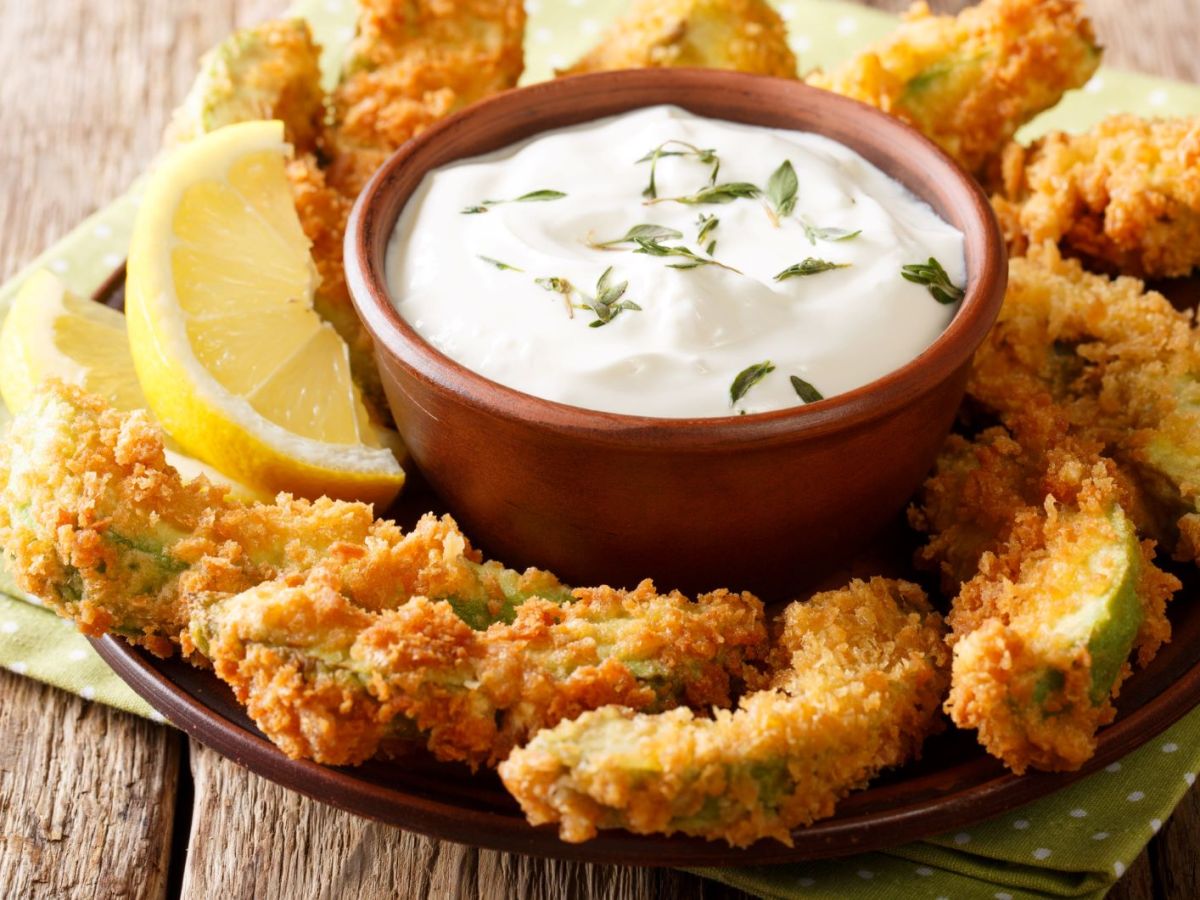 Frittierte Avocado-St&uuml;cke mit Dip auf einer Platte angerichtet.