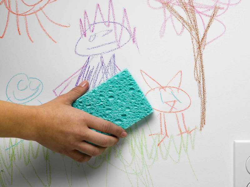Person macht mit einem Schwamm die Wand sauber, auf der ein Kind gemalt hat.