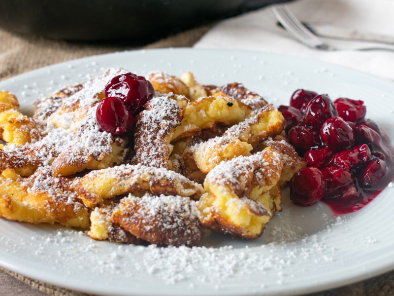 Kaiserschmarrn mit hei&szlig;en Kirschen auf einem wei&szlig;en Teller.