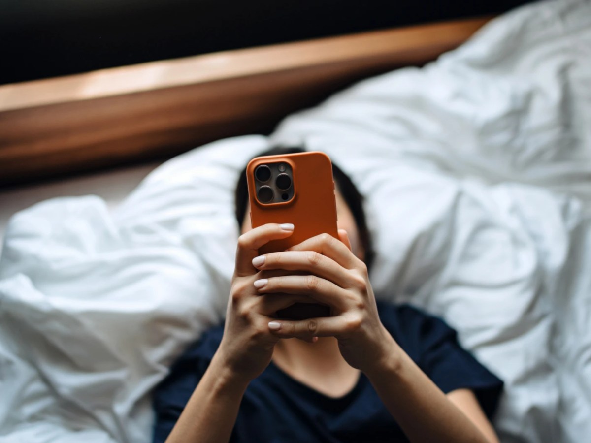 Frau liegt auf dem Bett und schaut auf ihr Smartphone