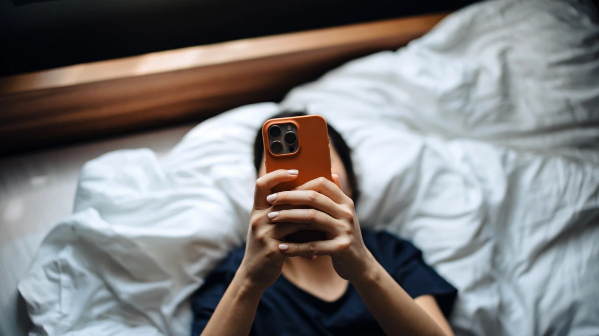 Frau liegt auf dem Bett und schaut auf ihr Smartphone