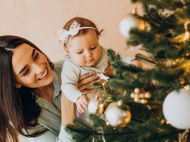 Mutter mit ihrem Baby schm&uuml;ckt den Weihnachtsbaum