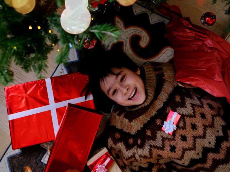 Junge im Teenageralter liegt auf dem Boden neben dem Weihnachtsbaum, umgeben von Weihnachtsgeschenken.
