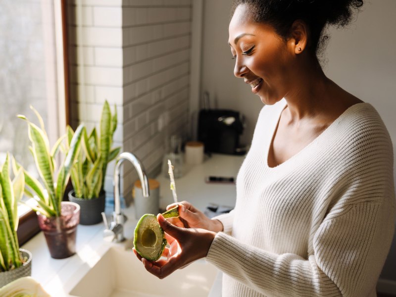 Erwachsene sch&ouml;ne afrikanische l&auml;chelnde schwangere Frau sch&auml;lt Avocado