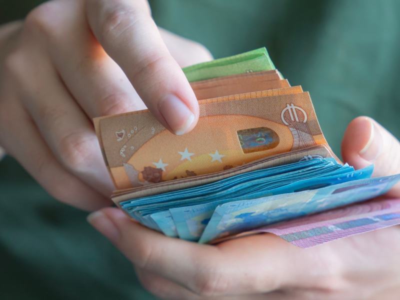 Eine Hand z&auml;hlt einen dicken Stapel Euro-Geldscheine in verschiedenen Farben, mit Fokus auf einen 50-Euro-Schein.