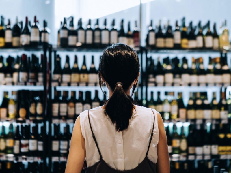 Frau steht vor einem Regal mit Weinflaschen im Supermarkt.