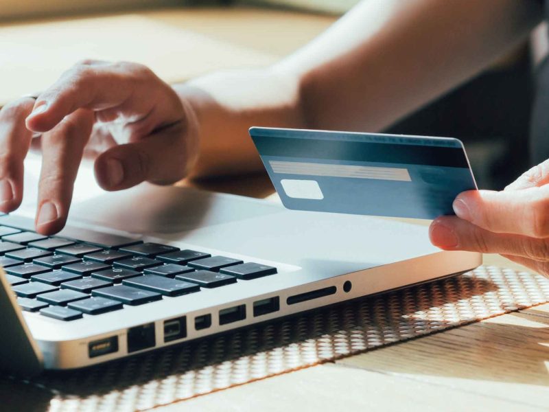 Frau tippt mit einer Hand auf dem Laptop und h&auml;lt in der anderen Hand ihre Bankkarte.