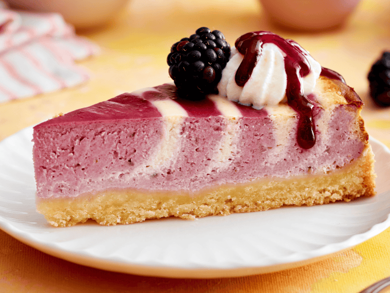 Ein St&uuml;ck K&auml;sekuchen mit Zebramuster und Brombeeren.