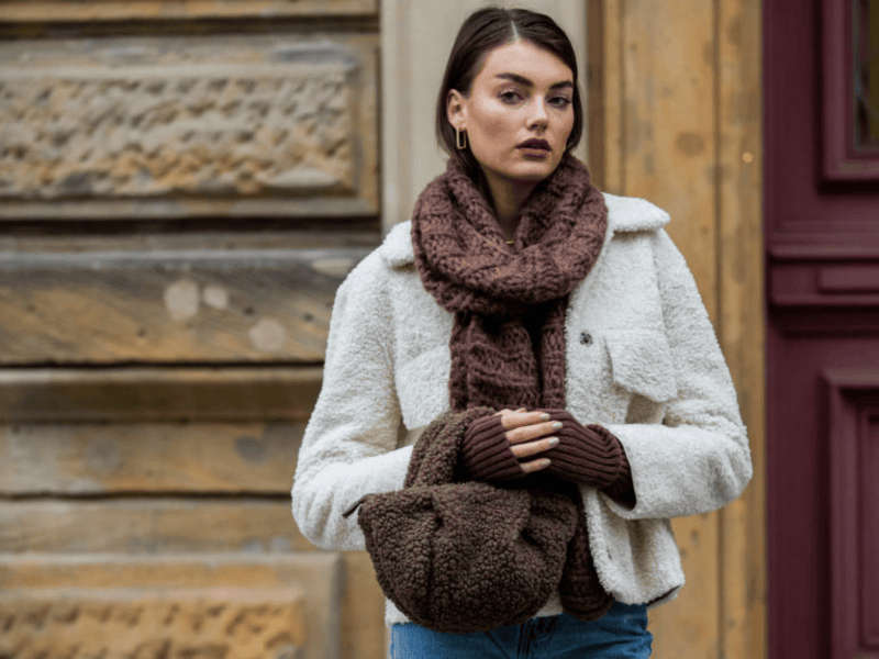Celine Bethmann mit weißer Jacke und Teddy-Tasche vor Häuserwand.