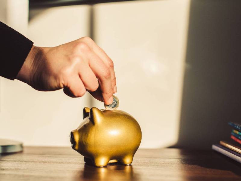 Person wirft einen Euro in ein goldenes Sparschwein.