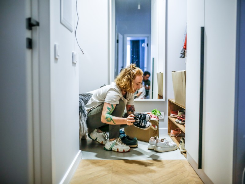 Frau kniet im Flur vor Schuhschrank