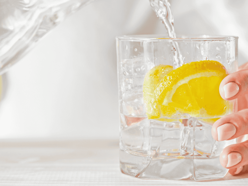 Frau gie&szlig;t Glas Wasser mit Zitrone ein.
