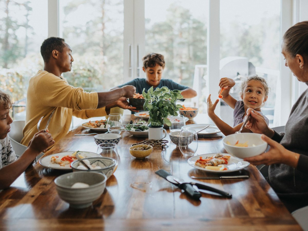 5-köpfige Familie sitzt zusammen am Tisch und isst.