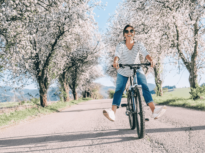 Frau strahlend auf dme Fahrrad umgeben von einer Kirschbl&uuml;tenbaumallee