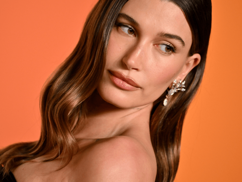 Hailey Bieber posiert in Bandeaukleid vor knalligem Hintergrund