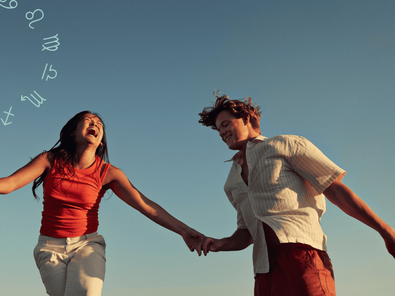 Frau und Mann halten sich an der Hand und lachen zusammen vor blauem Himmel