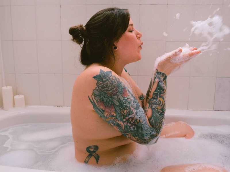 Junge Frau sitzt in der Badewanne voller Schaum.