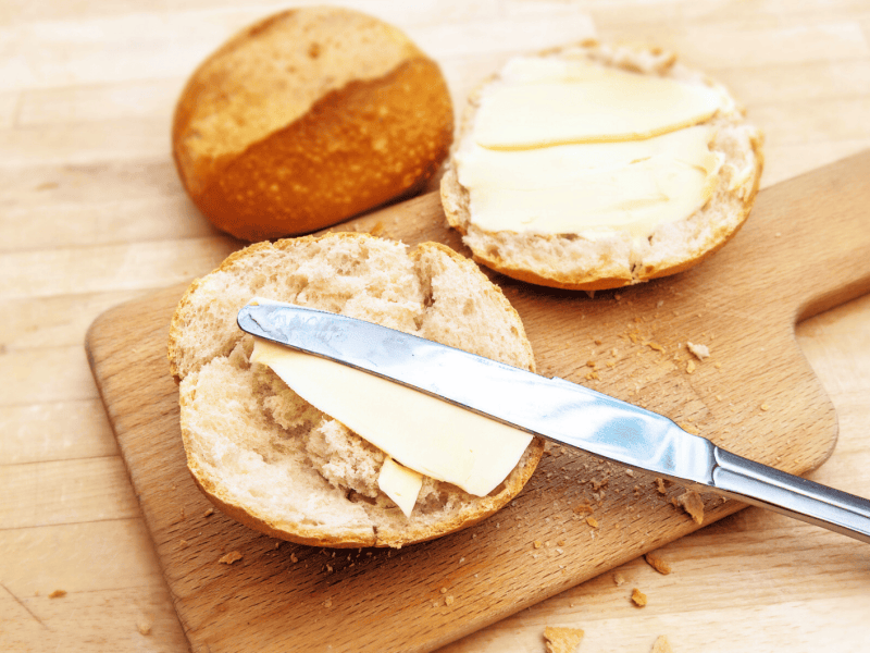 Aufgeschnittenes Br&ouml;tchen auf einem Holzbrettchen, mit Butter bestrichen.