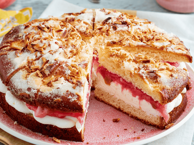 Gef&uuml;llter Butterkuchen mit Sahne und Rhabarber auf rosanem Teller.
