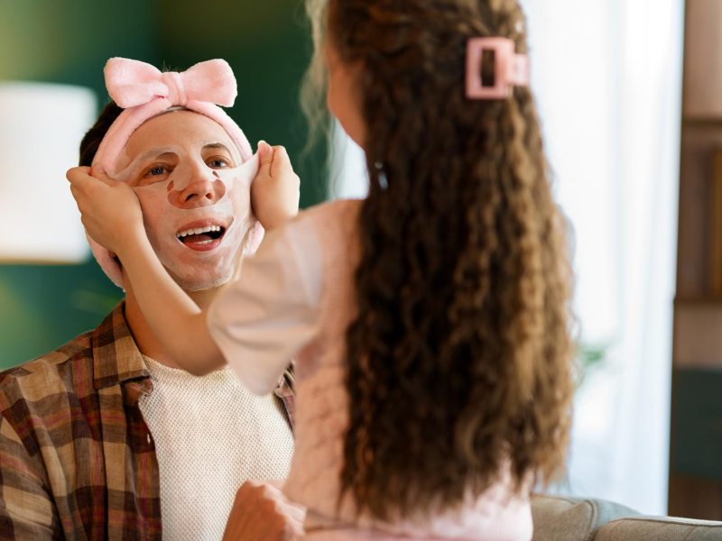 Kleine Tochter zieht ihrem Vater eine Gesichtsmaske auf.