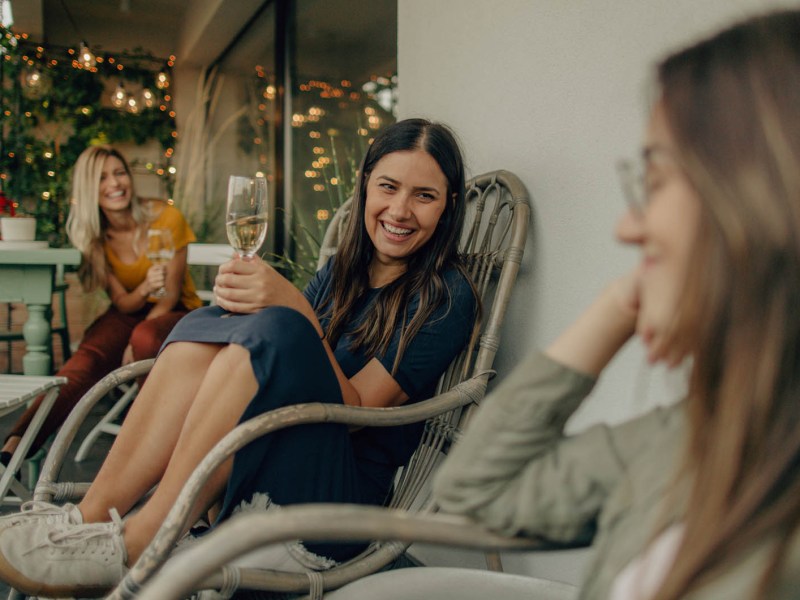 Drei Frauen sitzen im Sommer entspannt auf der Terrasse und unterhalten sich.
