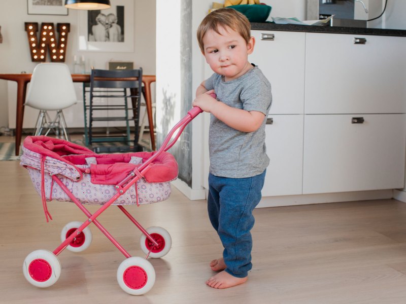 Kleiner Junge spielt mit Puppenwagen in der Küche.
