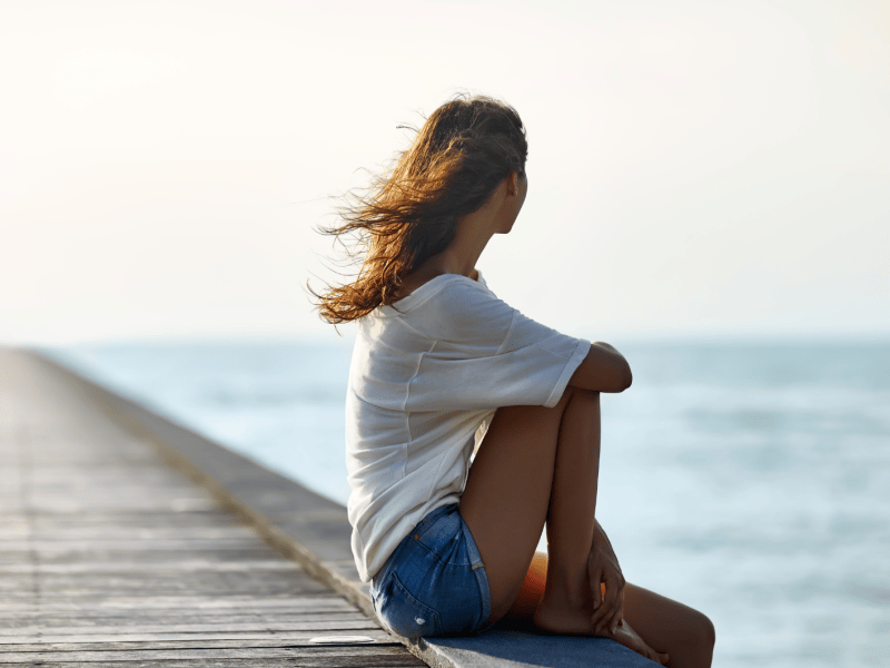 Frau in einem weißen T-Shirt sitzt auf einem Holzsteg am Meer