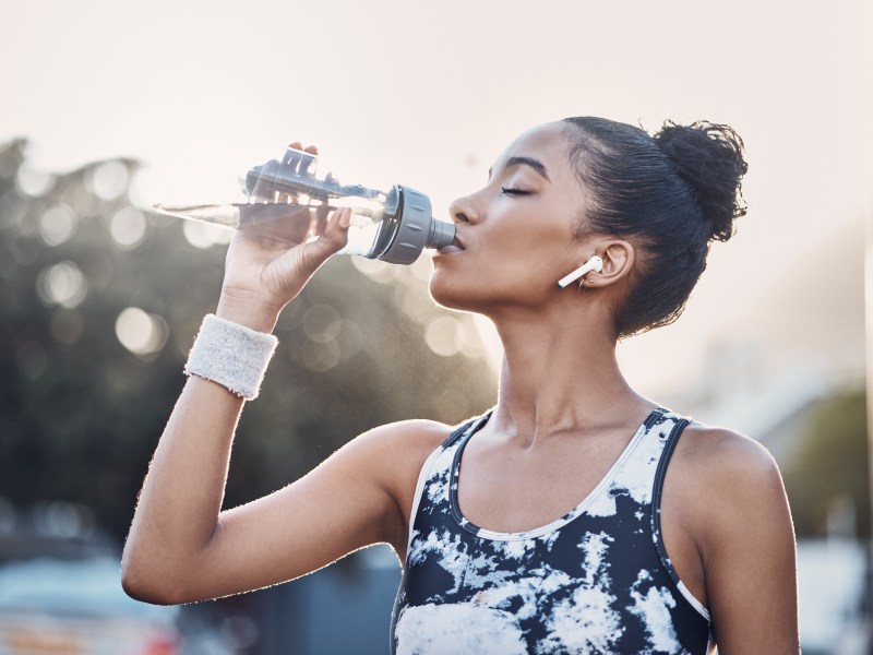 Weibliche Person, Outdoor und &Uuml;bung Pause mit Flasche Wasser, st&auml;dtische Umgebung und Kopfh&ouml;rer f&uuml;r Sport Musik