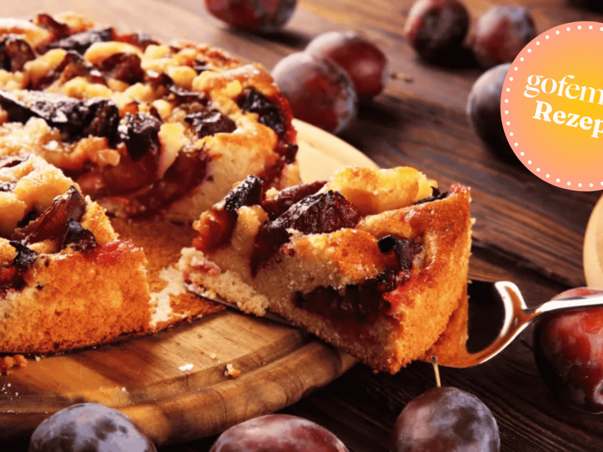 Pflaumenkuchen aus der Springform auf einem runden Holzbrett.