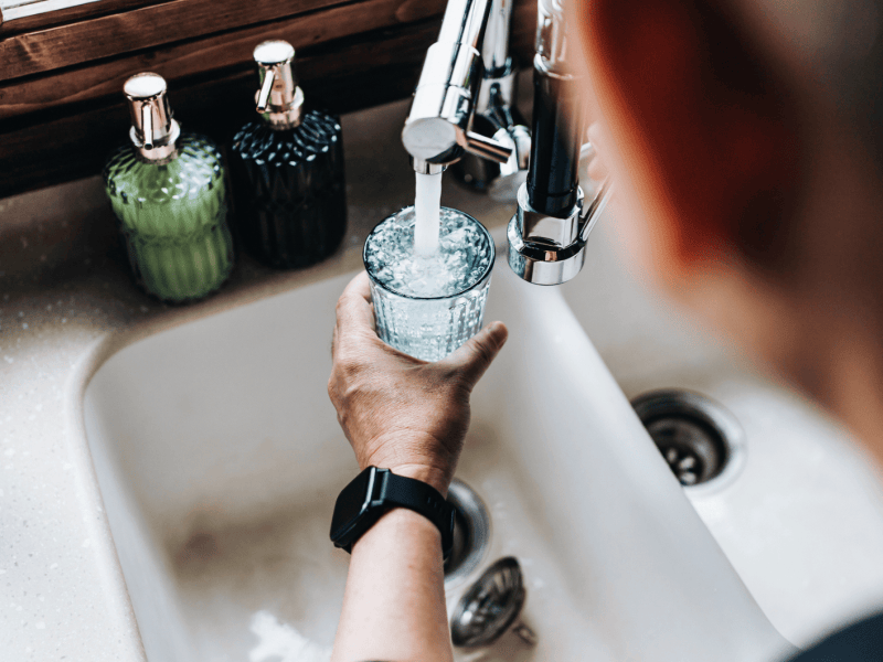 Mann f&uuml;llt Wasser aus Hahn in Glas.