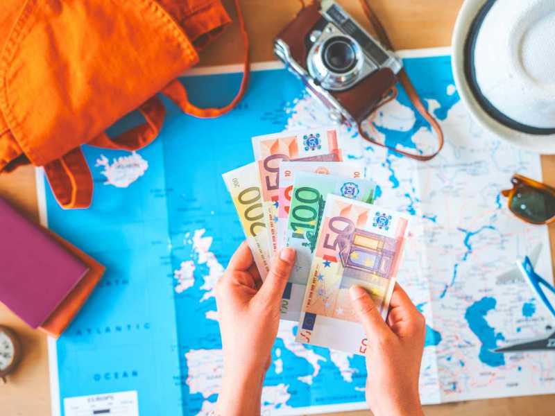 Frau h&auml;lt Geld auf Reisehintergrund.