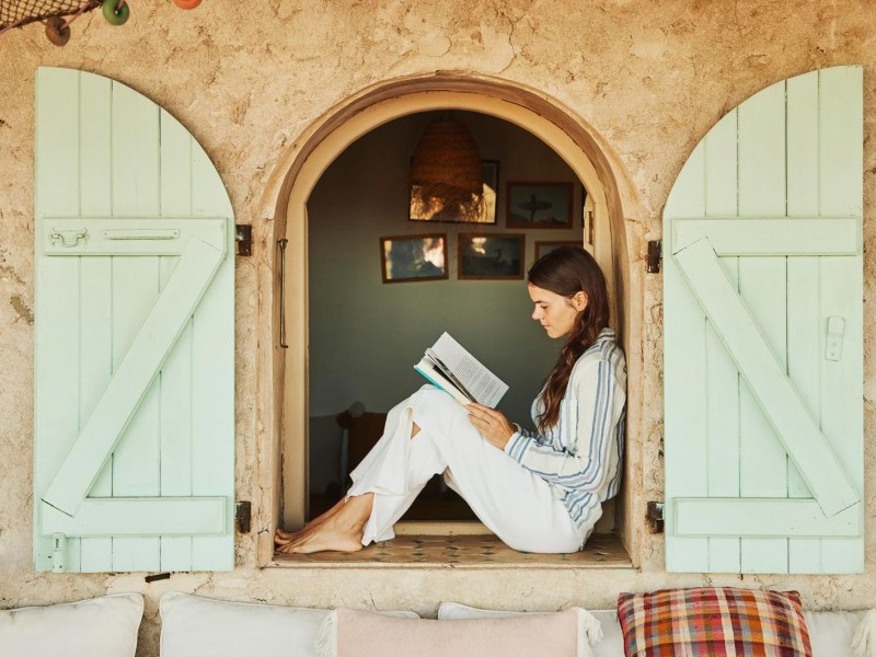 Junge Frau sitzt am Fenster und liest ein Buch, Urlaubsatmosph&auml;re