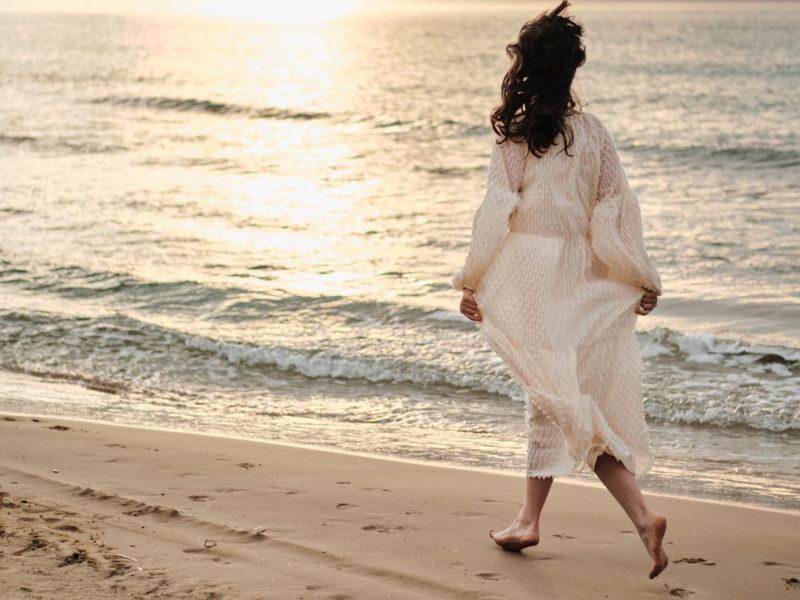 Frau in weißem Kleid läuft am Strand entlang