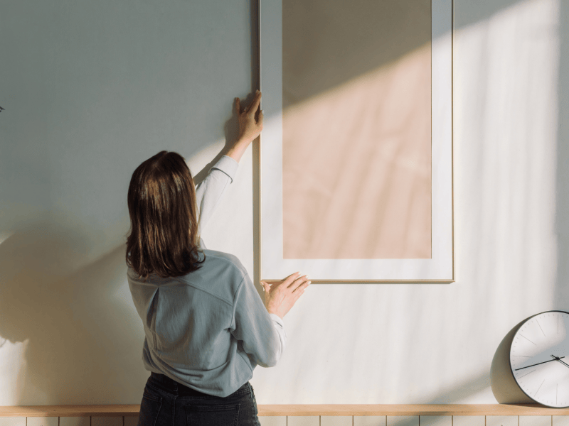 Frau dekoriert ihre Wand mit hellem Bilderrahmen.