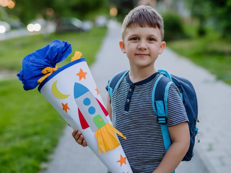 Junge posiert mit Schult&uuml;t drau&szlig;en.